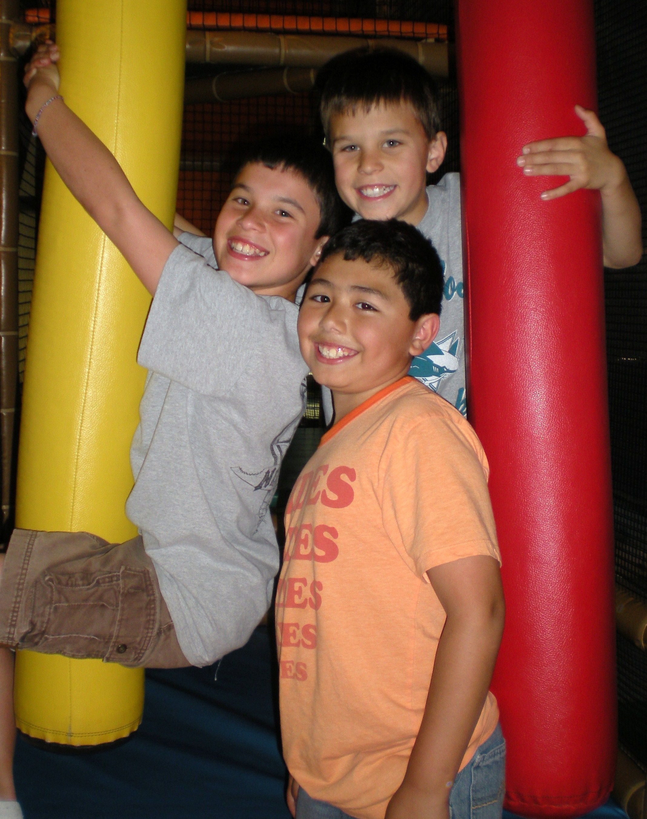 Three smiling kids hanging off the padded posts inside a Safari Run play structure