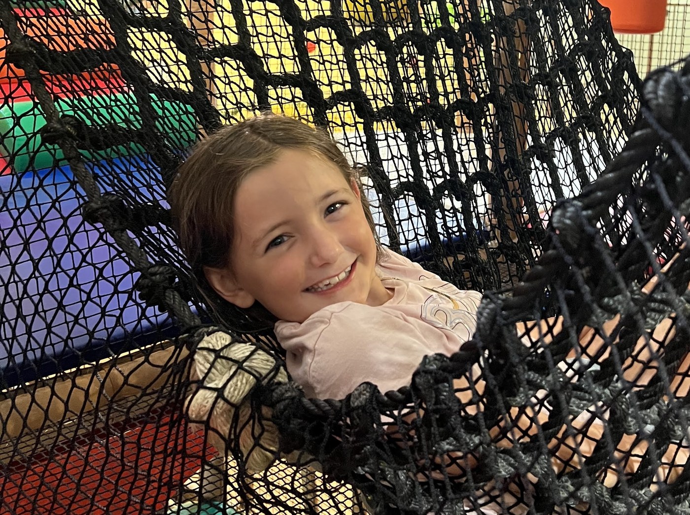 A smiling girl lounging in a black netted hammock inside the Safari Run play structure