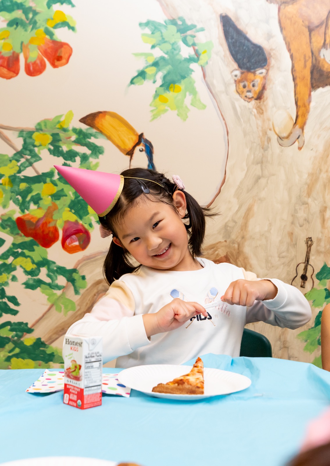 A girl in a pink party hat smiling at a birthday party table at Safari Run